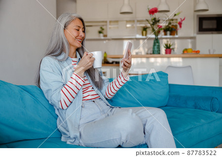 Woman with cup of coffee using cellphone at home 87783522