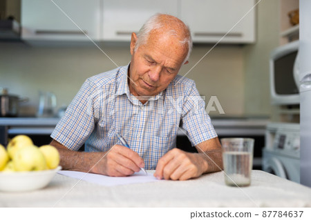 The old man is writing a letter at the table 87784637