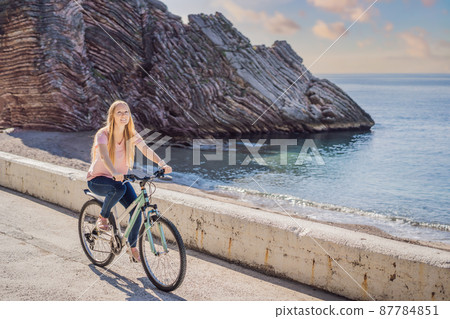 Woman tourist on a bicycle explores Budva in Montenegro. Cycling in Montenegro concept Woman tourist on a bicycle explores Budva in Montenegro. Cycling in Montenegro concept 87784851
