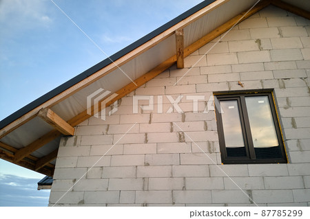 Unfinished house with aerated lightweight concrete walls and wooden roof frame covered with metallic tiles under construction 87785299