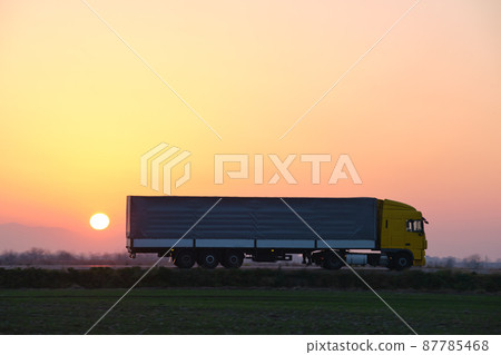 Semi-truck with cargo trailer driving on highway hauling goods in evening. Delivery transportation and logistics concept 87785468