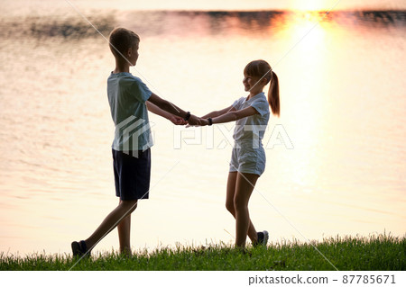 Happy siblings standing together holding hands in summer park. Young children brother and sister relaxing outdoors. Family love and relationship concept 87785671