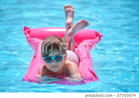 Happy child girl relaxing on inflatable air mattress in swimming pool on sunny summer day during tropical vacations. Summertime activities concept 87785674
