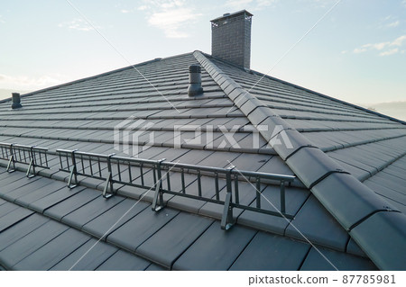 Closeup snow guard for safety in winter on house roof top covered with ceramic shingles. Tiled covering of building Closeup snow guard for safety in winter on house roof top covered with ceramic shingles. Tiled covering of building 87785981