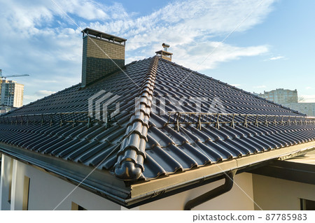 Closeup snow guard for safety in winter on house roof top covered with ceramic shingles. Tiled covering of building Closeup snow guard for safety in winter on house roof top covered with ceramic shingles. Tiled covering of building 87785983