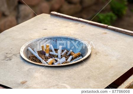 Close up of cigarettes butts in metal ashtray on street. Concept of many cigarette debris after smoking. Close up of cigarettes butts in metal ashtray on street. Concept of many cigarette debris after smoking. 87786008
