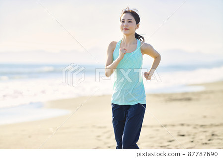 Young woman in sportswear running on a sandy beach 87787690