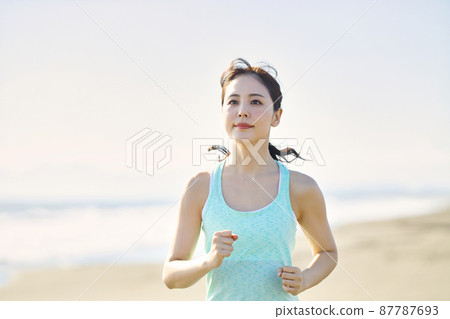 Young woman in sportswear running on a sandy beach 87787693