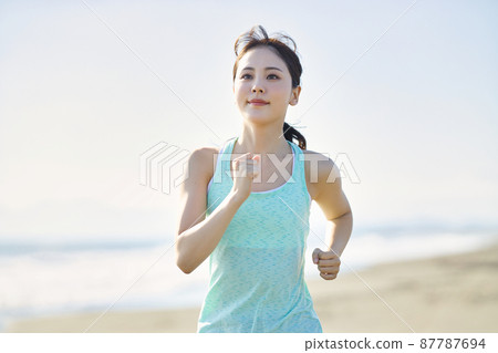 Young woman in sportswear running on a sandy beach 87787694