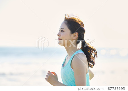 Young woman in sportswear running on a sandy beach 87787695