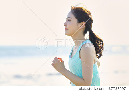 Young woman in sportswear running on a sandy beach 87787697