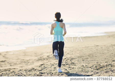 Young woman in sportswear running on a sandy beach 87788012