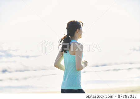 Young woman in sportswear running on a sandy beach 87788015