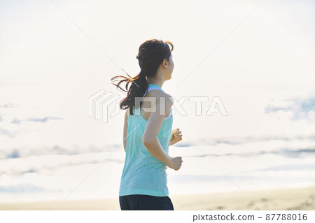 Young woman in sportswear running on a sandy beach 87788016
