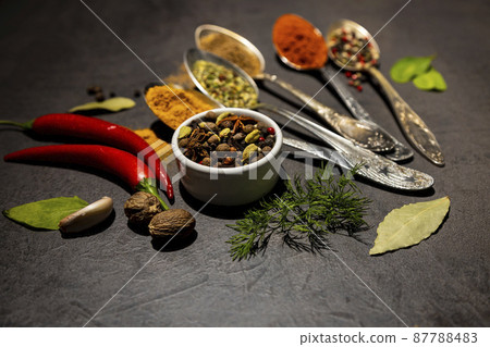Culinary condiments. Various herbs and spices with old metal spoons on a dark background. Nutmeg, chili peppers 87788483