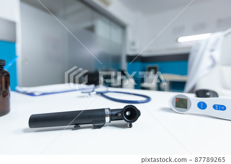 Close up of medical otoscop standing on table in empty doctor office Close up of medical otoscop standing on table in empty doctor office 87789265