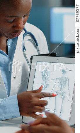 Woman working as doctor holding tablet with skeleton image Woman working as doctor holding tablet with skeleton image 87789577