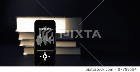 Audio book education. Phone screen with audio book app on paper books black background. Online learning, home school concept. Audio book education. Phone screen with audio book app on paper books black background. Online learning, home school concept. 87789584