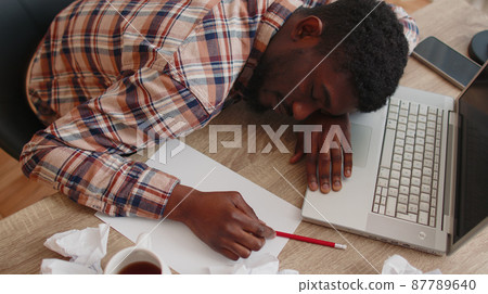Tired man at home office falling asleep on table with laptop computer, crumpled sheets of paper 87789640
