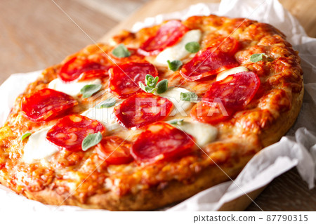 Pizza with pepperoni sausage and cheese on a wooden board on a wooden background Pizza with pepperoni sausage and cheese on a wooden board on a wooden background 87790315