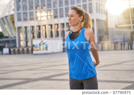 Attractive middle aged woman in sportswear stretching her arms, warming up while getting ready for workout in the city Attractive middle aged woman in sportswear stretching her arms, warming up while getting ready for workout in the city 87790975
