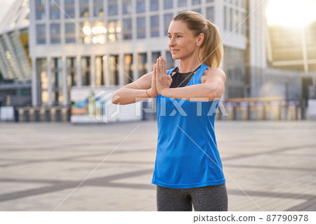 Relaxed middle aged woman in sportswear stretching her arms, getting ready for workout in the city Relaxed middle aged woman in sportswear stretching her arms, getting ready for workout in the city 87790978