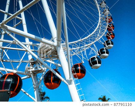 Ferris wheel in the city against the blue sky. carousel for riding. attraction for a sightseeing tour of the city. red round cabins with black tinted glass were made for sitting tourists 87791110