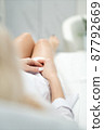 Skinny woman with beautiful legs with well-groomed leather and crossed arms lies on a white beauty table 87792669