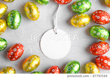 Round white Easter tag mockup with Happy Easter chocolate easter eggs on grey stone background 87793584