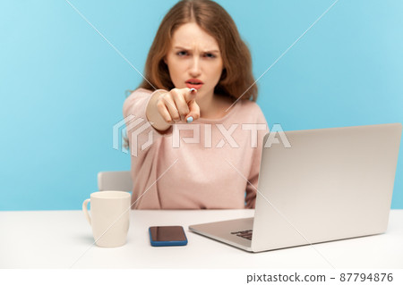 Hey you. Irritated angry businesswoman in casual clothes pointing finger to camera, scolding and choosing guilty, sitting at workplace home office. indoor studio shot isolated on blue background Hey you. Irritated angry businesswoman in casual clothes pointing finger to camera, scolding and choosing guilty, sitting at workplace home office. indoor studio shot isolated on blue background 87794876
