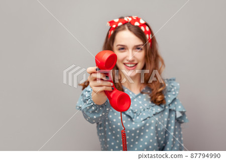 Take it, answer call. Charming happy pinup girl giving phone handset looking at camera, smiling looking friendly joyful, helpful contact center, customer support. studio shot isolated gray background, 87794990
