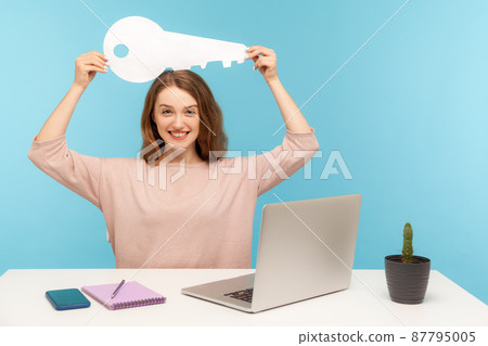 Positive emotions about property purchase, rental office. Amazing woman sitting at workplace with laptop and holding big paper key over head, pleased with real estate agency service. indoor isolated Positive emotions about property purchase, rental office. Amazing woman sitting at workplace with laptop and holding big paper key over head, pleased with real estate agency service. indoor isolated 87795005