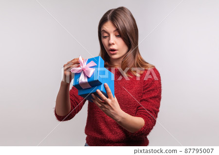Portrait of curious amazed brunette girl in shaggy sweater opening gift box, looking inside with surprised expression, unwrapping birthday present. indoor studio shot isolated on gray background Portrait of curious amazed brunette girl in shaggy sweater opening gift box, looking inside with surprised expression, unwrapping birthday present. indoor studio shot isolated on gray background 87795007