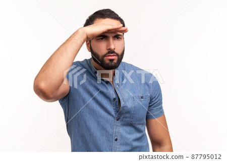 Thoughtful bearded man looking far away at distance with hand over head, attentively searching for bright future. Indoor studio shot isolated on white background 87795012