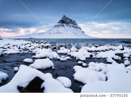 Kirkjufell mountain, Iceland. Winter landscape. The mountain and the ocean. Snow and ice. Kirkjufell mountain, Iceland. Winter landscape. The mountain and the ocean. Snow and ice. 87795105