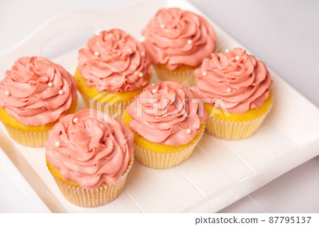 Fresh and delicious cupcakes with yogurt cream. Cakes with cream on table. Muffin with cream. Ready-made pastry, dessert for serving. Indoor studio shot isolated on pink background. 87795137