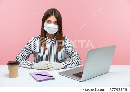 Serious businesswoman sitting safe healthy with hygienic face mask and protective gloves during quarantine, looking at camera. Working at home office in self-isolation, coronavirus outbreak. indoor Serious businesswoman sitting safe healthy with hygienic face mask and protective gloves during quarantine, looking at camera. Working at home office in self-isolation, coronavirus outbreak. indoor 87795156