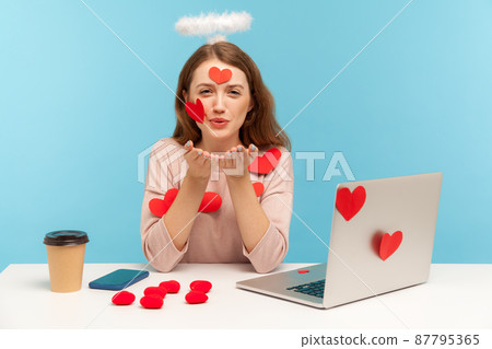 Angelic woman with kind expression sitting at workplace office, all covered with sticker love hearts, sending romantic sensual air kiss, full of valentine's day greetings. indoor studio shot, isolated Angelic woman with kind expression sitting at workplace office, all covered with sticker love hearts, sending romantic sensual air kiss, full of valentine's day greetings. indoor studio shot, isolated 87795365