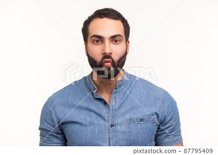 Funny comical man with beard in blue shirt folding lips pretending to be fish, making faces and having fun, good mood. Indoor studio shot isolated on white background 87795409