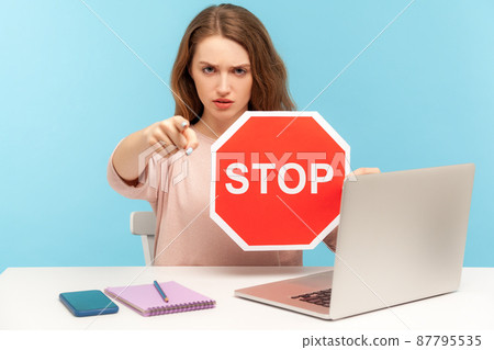 Angry woman boss, office employee at workplace, holding stop symbol and pointing to camera, showing red traffic sign, negative prohibition concept. indoor studio shot isolated on blue background Angry woman boss, office employee at workplace, holding stop symbol and pointing to camera, showing red traffic sign, negative prohibition concept. indoor studio shot isolated on blue background 87795535