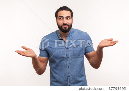 Puzzled clueless man with beard in blue shirt throwing up his hands looking at camera with uncertain expression, has no answers. Indoor studio shot isolated on white background Puzzled clueless man with beard in blue shirt throwing up his hands looking at camera with uncertain expression, has no answers. Indoor studio shot isolated on white background 87795695