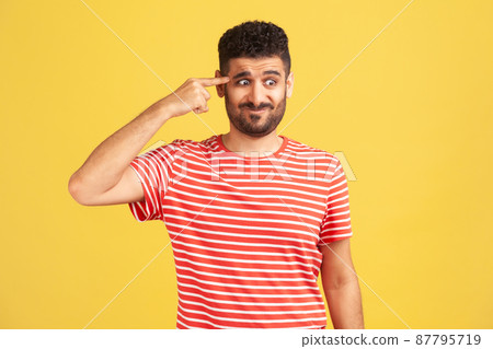 Crazy idea. Bearded man in red striped t-shirt showing stupid gesture, looking with condemnation and blaming for insane plan, dumb suggestion. Indoor studio shot isolated on yellow background 87795719