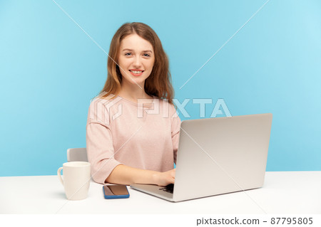 Happy positive beautiful businesswoman in casual clothes looking at camera with toothy smile, working on laptop at home office, doing freelance job. indoor studio shot isolated on blue background 87795805