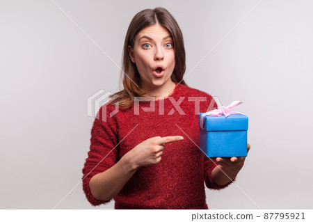 Surprised girl in shaggy sweater pointing decorated wrapped gift box and looking at camera with amazed expression, shocked by birthday present, bonus. indoor studio shot isolated on gray background Surprised girl in shaggy sweater pointing decorated wrapped gift box and looking at camera with amazed expression, shocked by birthday present, bonus. indoor studio shot isolated on gray background 87795921