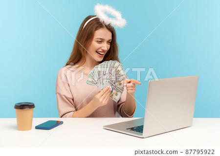 Make money on internet. Angelic rich woman with nimbus holding dollar banknotes and pointing laptop screen while talking on video call, encouraging to earn online. indoor studio shot, isolated 87795922
