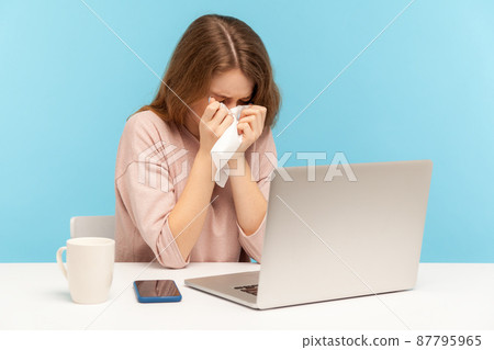 Depressed overworked female employee crying and wiping tears with tissue, feeling worried and desperate about job troubles, sitting at workplace home office. indoor studio shot, blue background 87795965