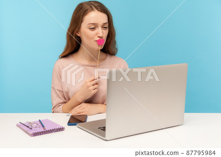 Beautiful happy woman covering her mouth with pink lips and looking at laptop screen, talking with boyfriend on video call, having online romantic date. indoor studio shot isolated on blue background 87795984