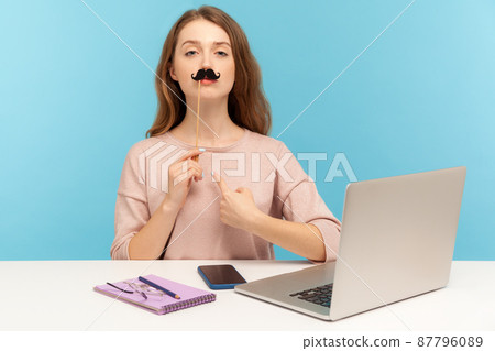 Funny arrogant woman office employee pointing herself, covering lips with fake paper moustache, imitating strict boss, humorous masquerade accessory. indoor studio shot isolated on blue background 87796089