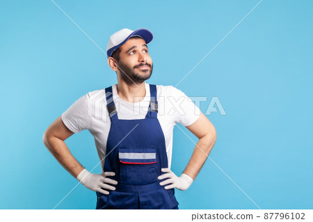 Thoughtful handyman in overalls looking up, dreaming with happy inspired expression, making wish. Profession of service industry, courier delivery, housekeeping maintenance. studio shot isolated Thoughtful handyman in overalls looking up, dreaming with happy inspired expression, making wish. Profession of service industry, courier delivery, housekeeping maintenance. studio shot isolated 87796102