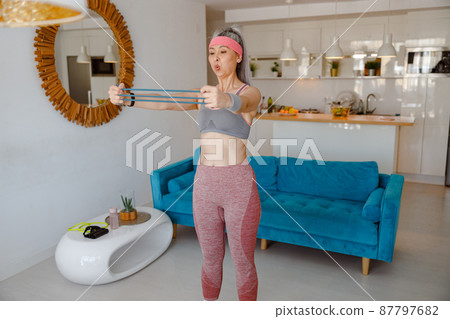 Sporty woman using arm resistance band during home workout 87797682